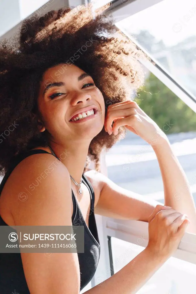 Happy young woman with afro hairstyle at bedroom window, head and shoulder portrait