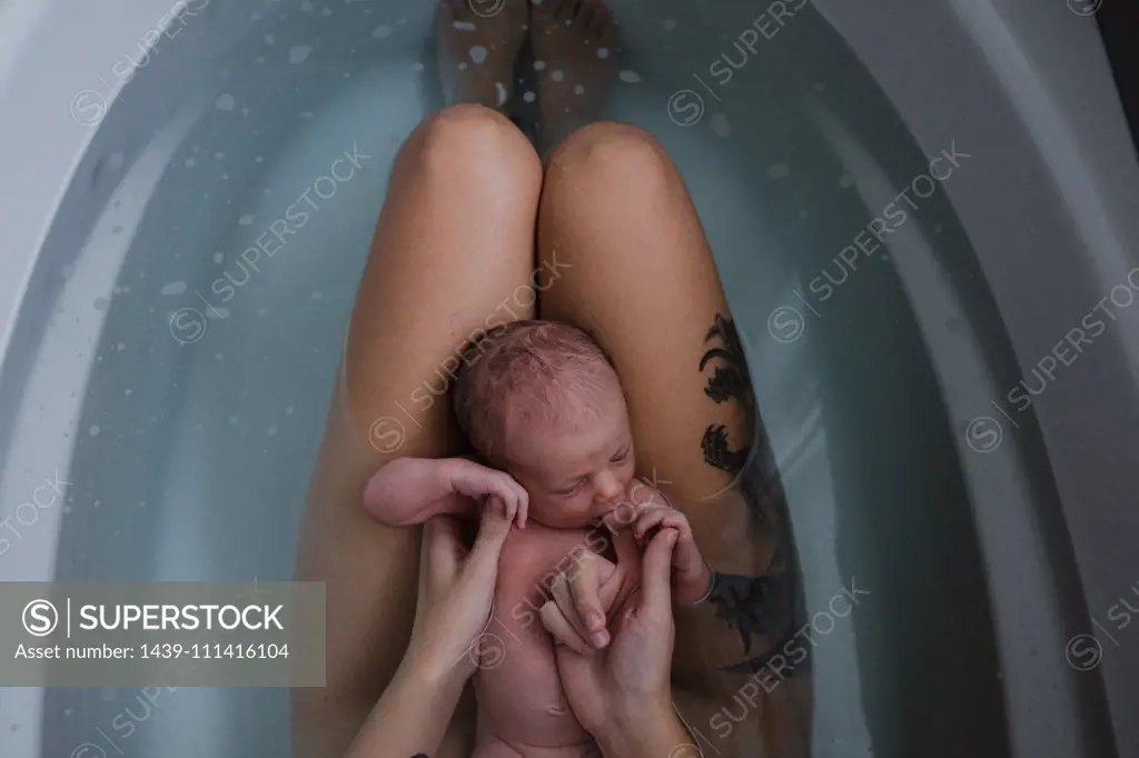 Mother with baby son on her lap in bath, cropped overhead view