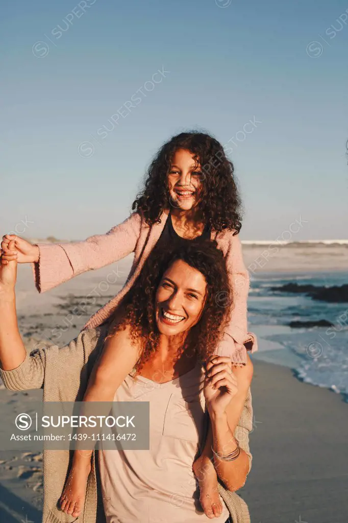 Mother giving daughter piggyback ride on beach