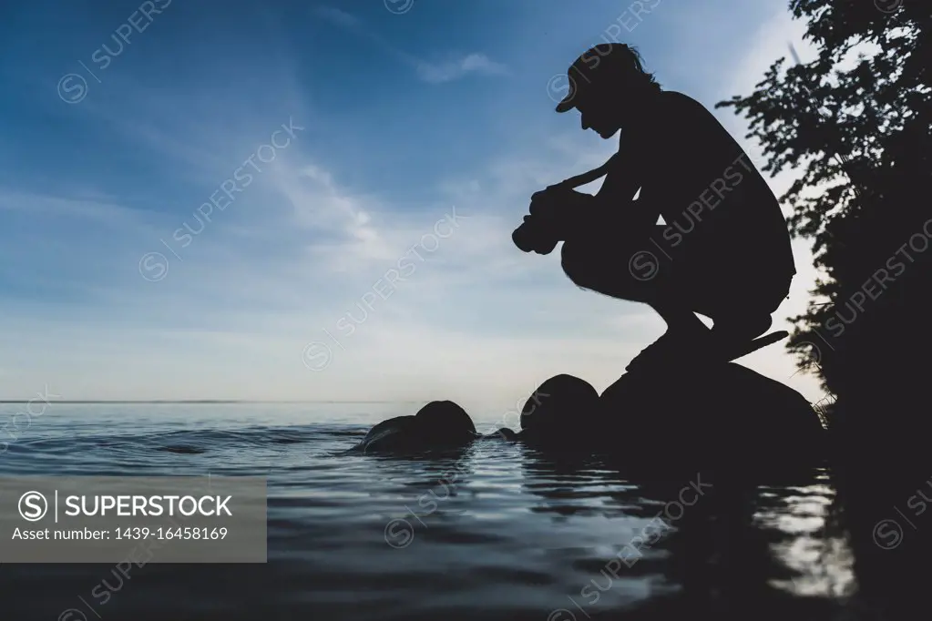 Silhouette of man crouching by the shore of a lake