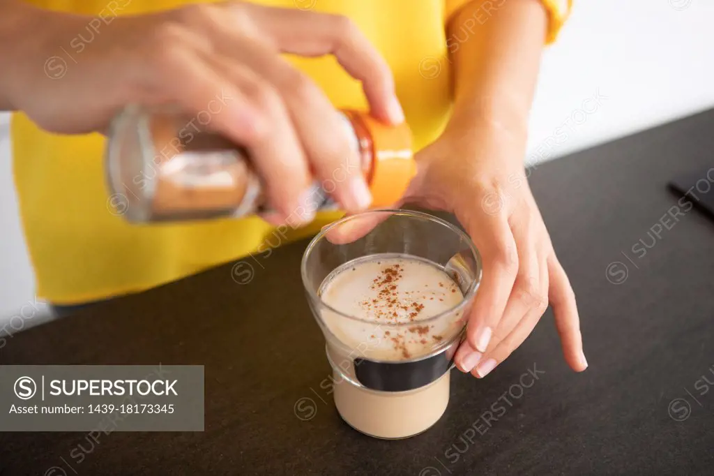 Portugal, Lisbon, Close-up of woman's hands sprinkling coffee with cinnamon