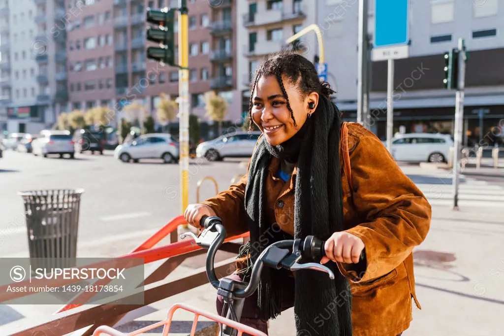 Smiling young woman with bicycle on city street