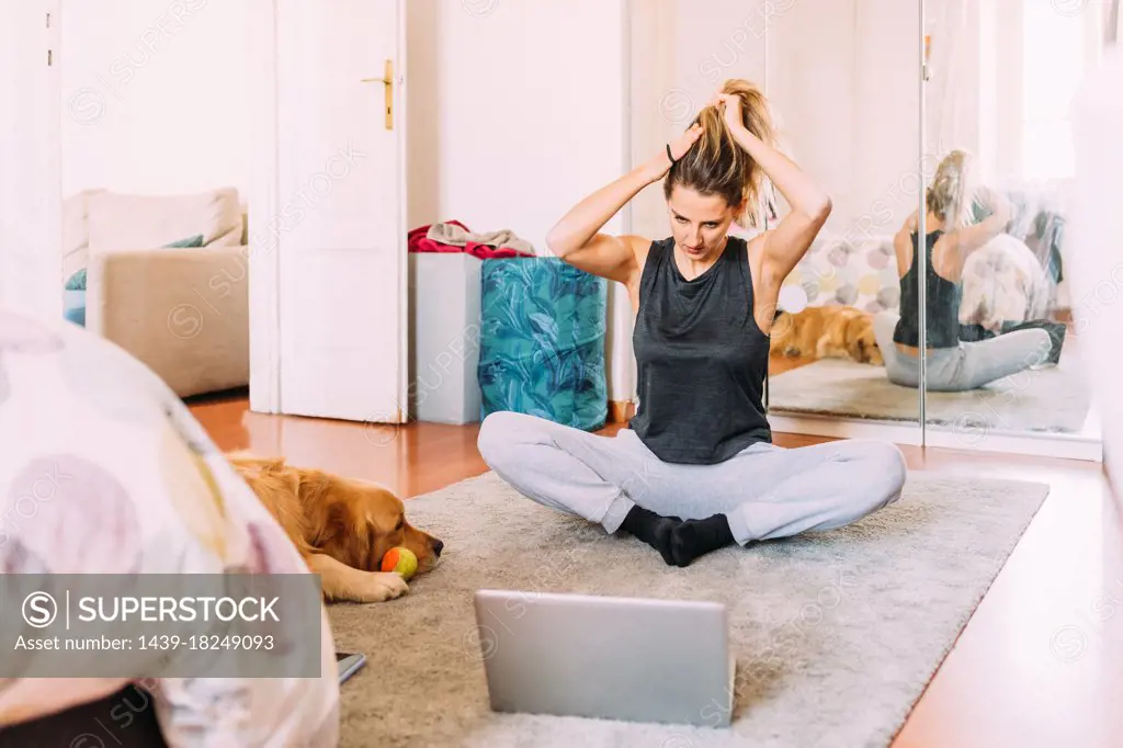 Italy, Young woman stretching in front of laptop on floor