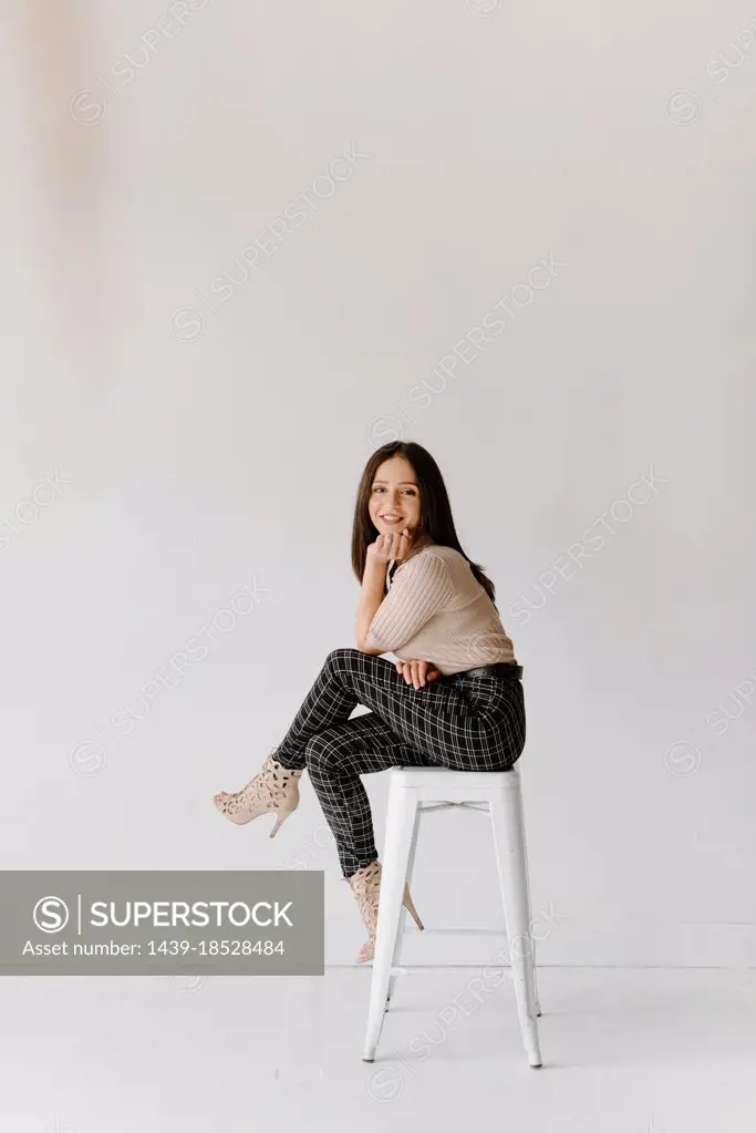 Studio shot of young woman sitting on stool