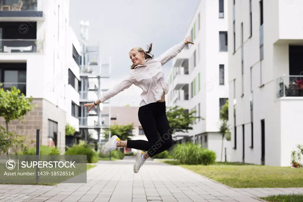 Smiling young woman jumping in modern neighborhood