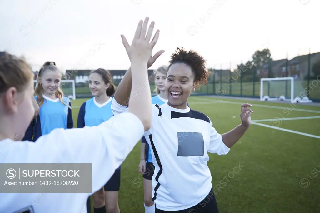 UK, Female soccer team members giving high five in field