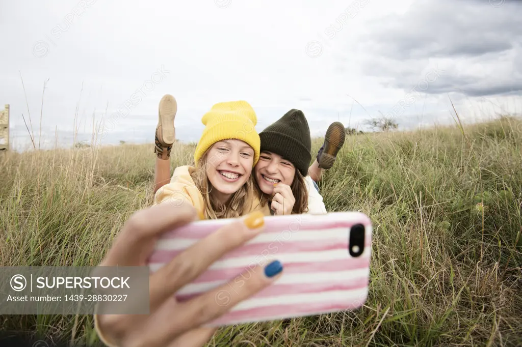 Smiling girl friends (10-11) lying in grass and taking selfie