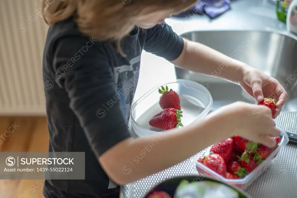 Young boy cutting healthy strawberries with help from his mum