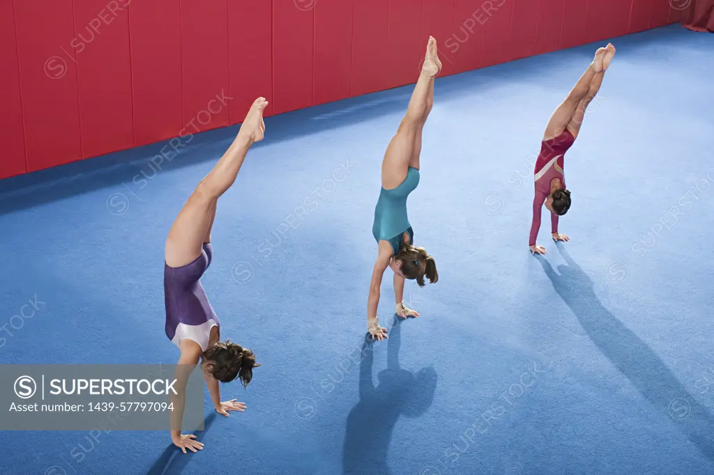 Three gymnasts perfecting their handstands in a vibrant gymnasium