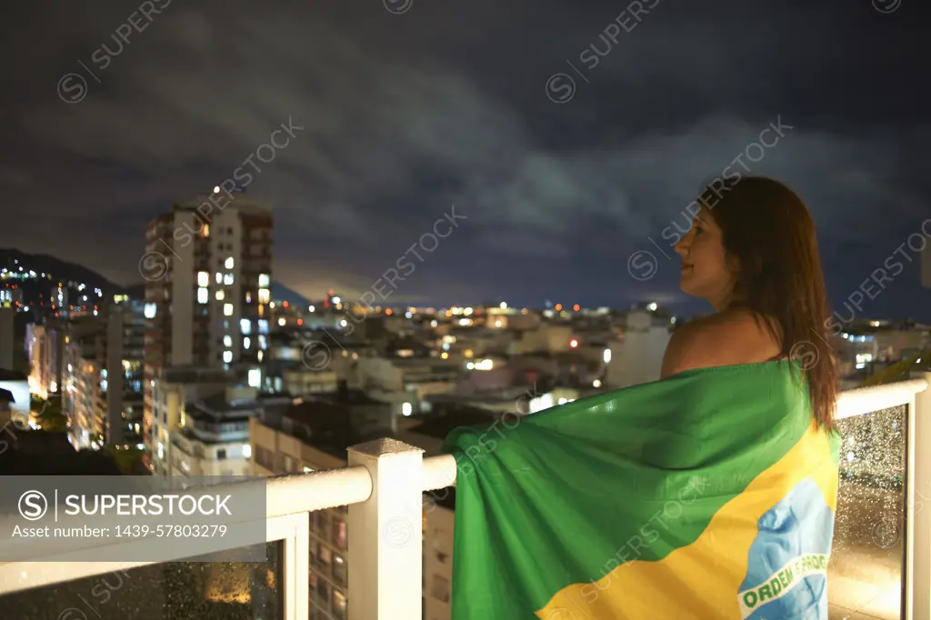 Mature woman gazing from balcony at night, Rio De Janeiro, Brazil