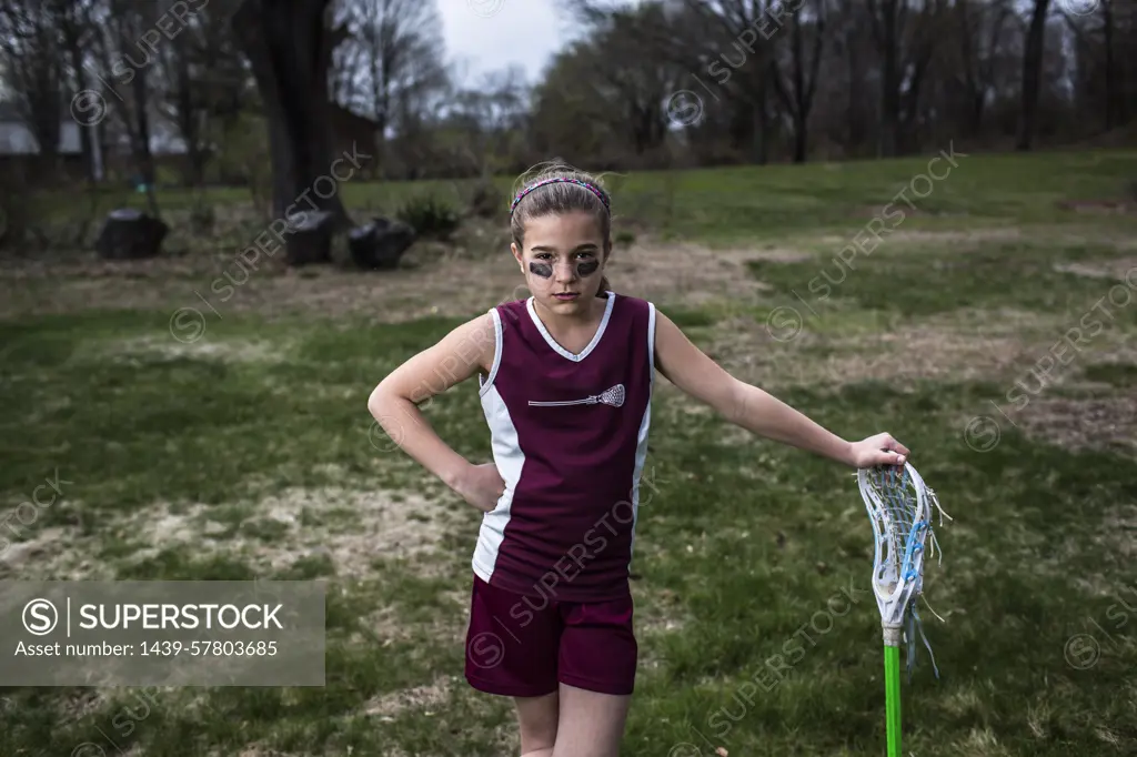 Girl wearing lacrosse uniform, leaning against lacrosse stick