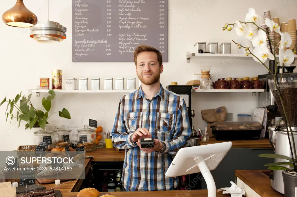 Portrait of cafe waiter with card machine behind counter