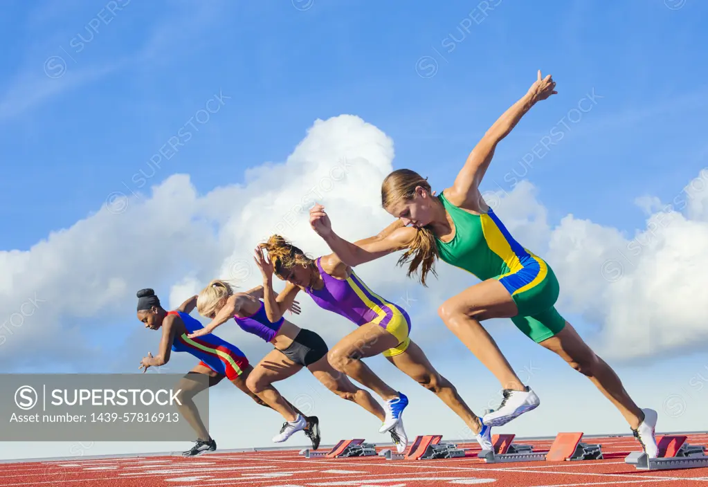 Four female athletes on athletics track, starting race