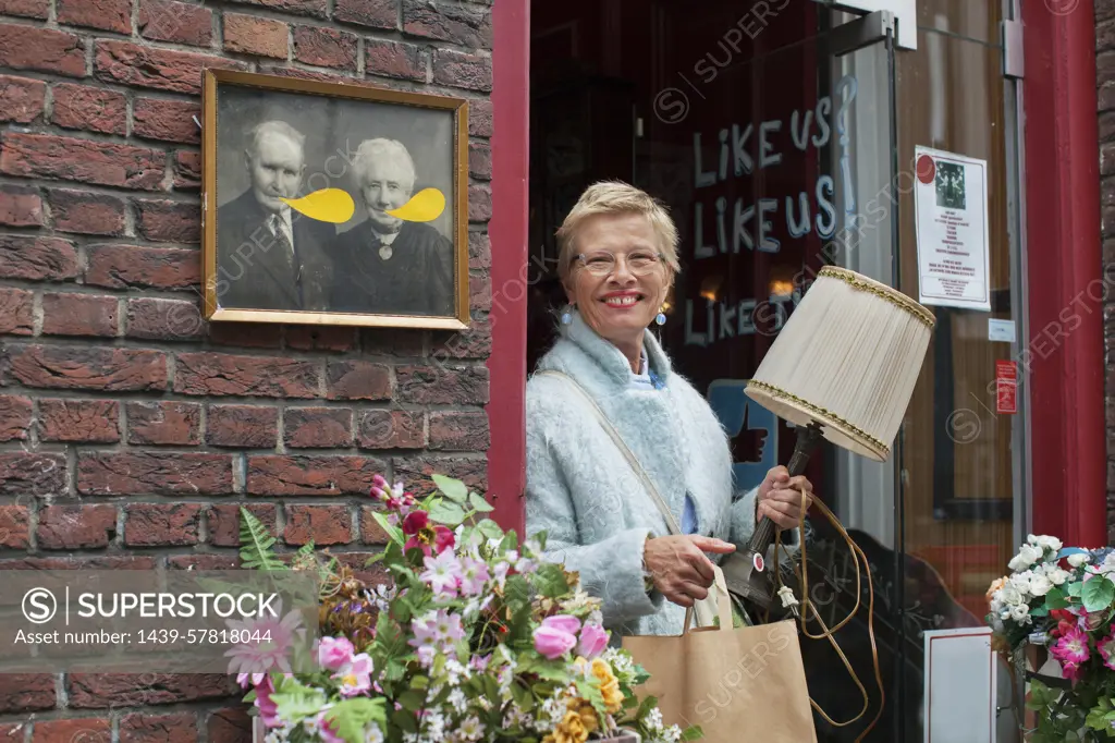 Mature female customer carrying lamp and shopping bag outside vintage shop