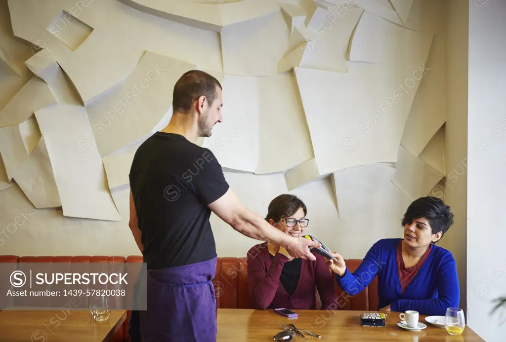 Waiter handing credit card machine to woman in restaurant