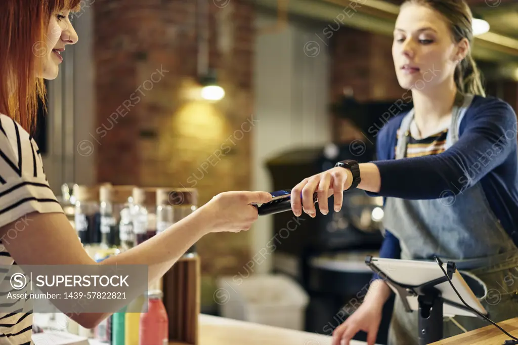 Female barista taking smartphone contactless payment from coffee shop customer