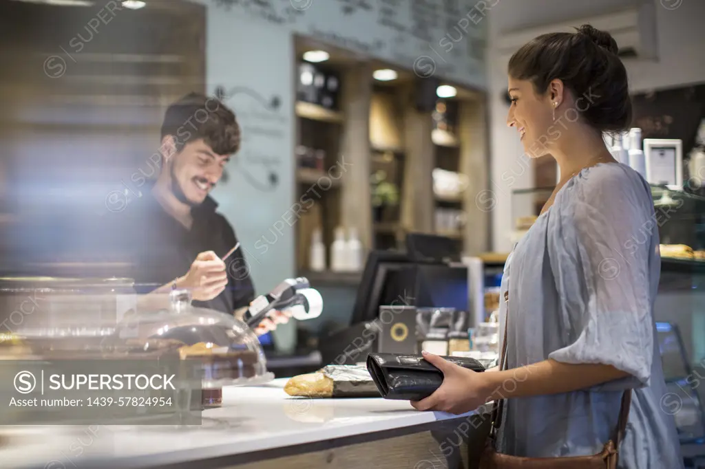 Barista calculating bill for female customer at cafe counter