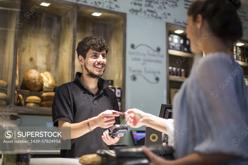 Barista handing credit card to female customer at cafe counter