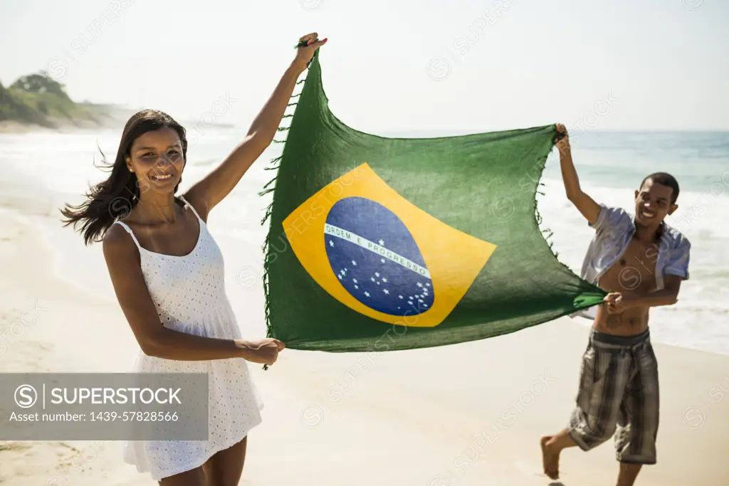 Young couple holding up Brazilian flag, Arpoador beach, Rio De Janeiro, Brazil