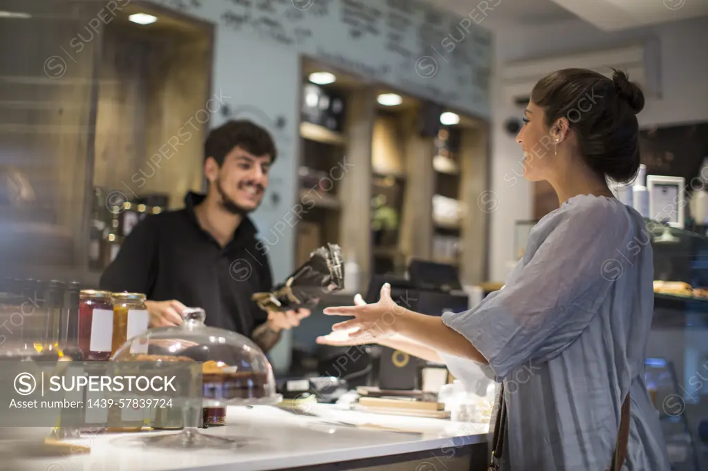 Barista handing baguette to female customer at cafe counter