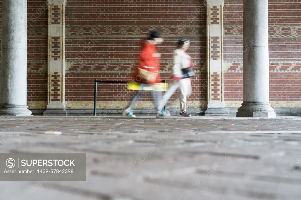 Blurred motion of people walking by brick wall, Amsterdam, Netherlands