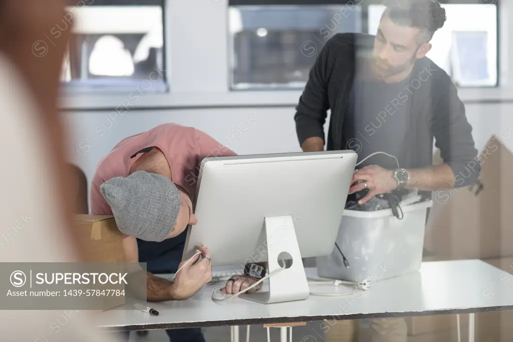 Two men working on a computer in an office setting.