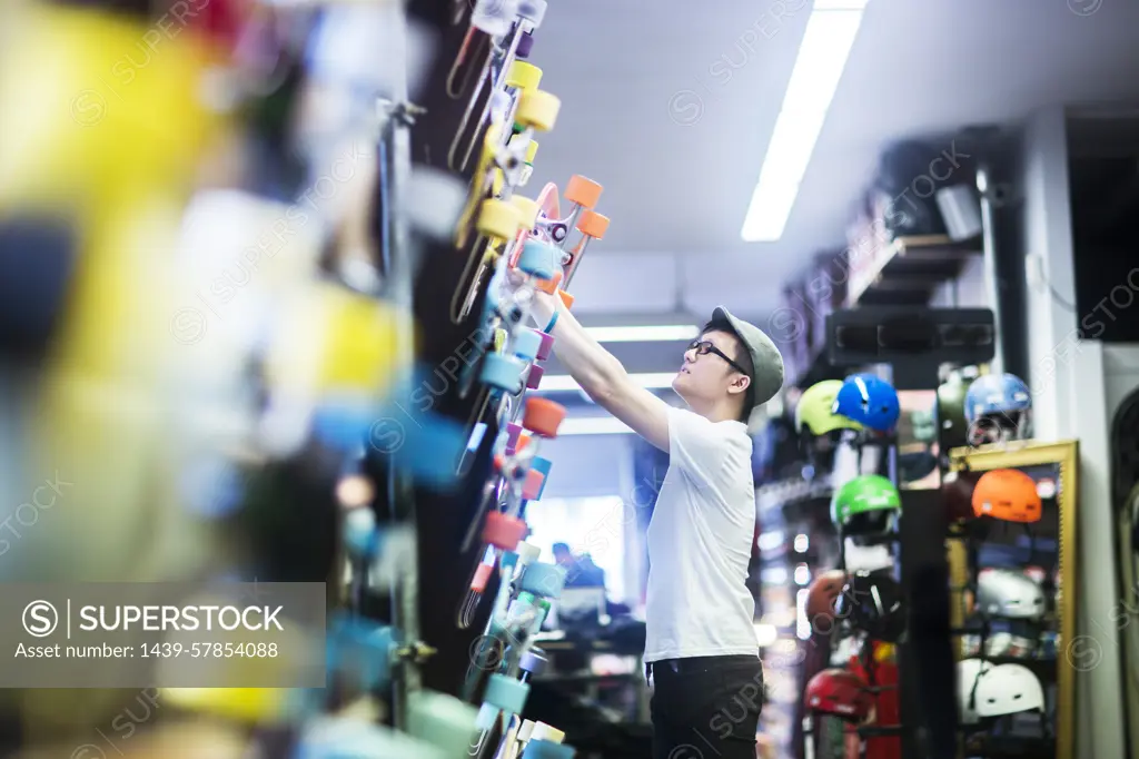 Young male skateboarder removing skateboard from wall in skateboard shop