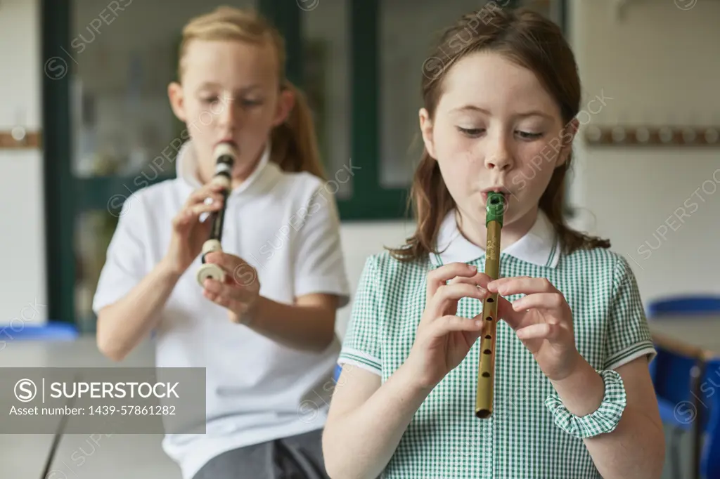 Two children practice playing the recorder during music class.