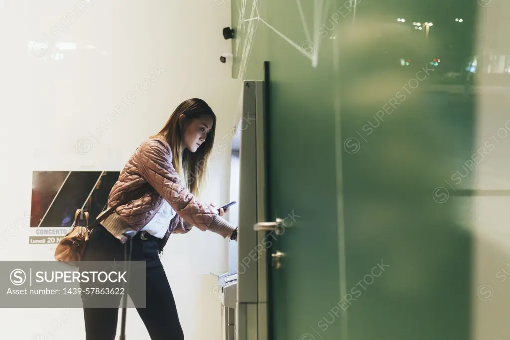 Young woman using machine to buy train ticket