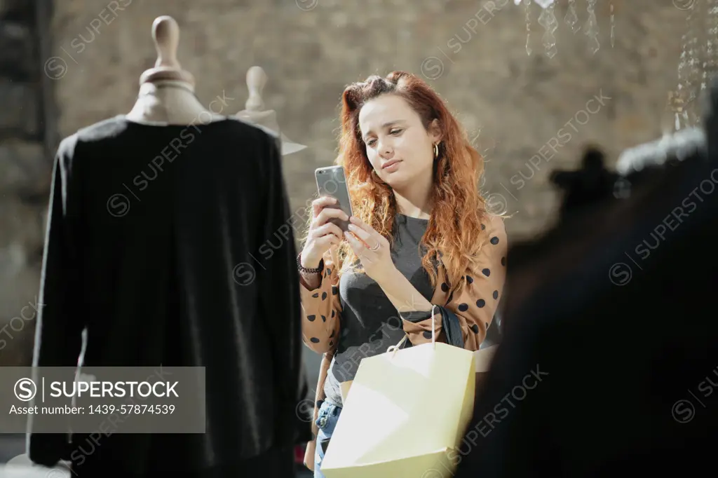 Female shopper taking photograph of top in front of fashion boutique