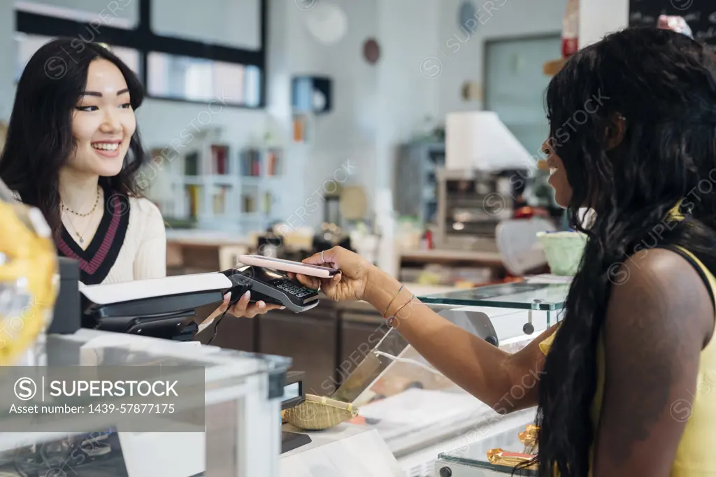 Young businesswoman making smartphone payment at cafe counter