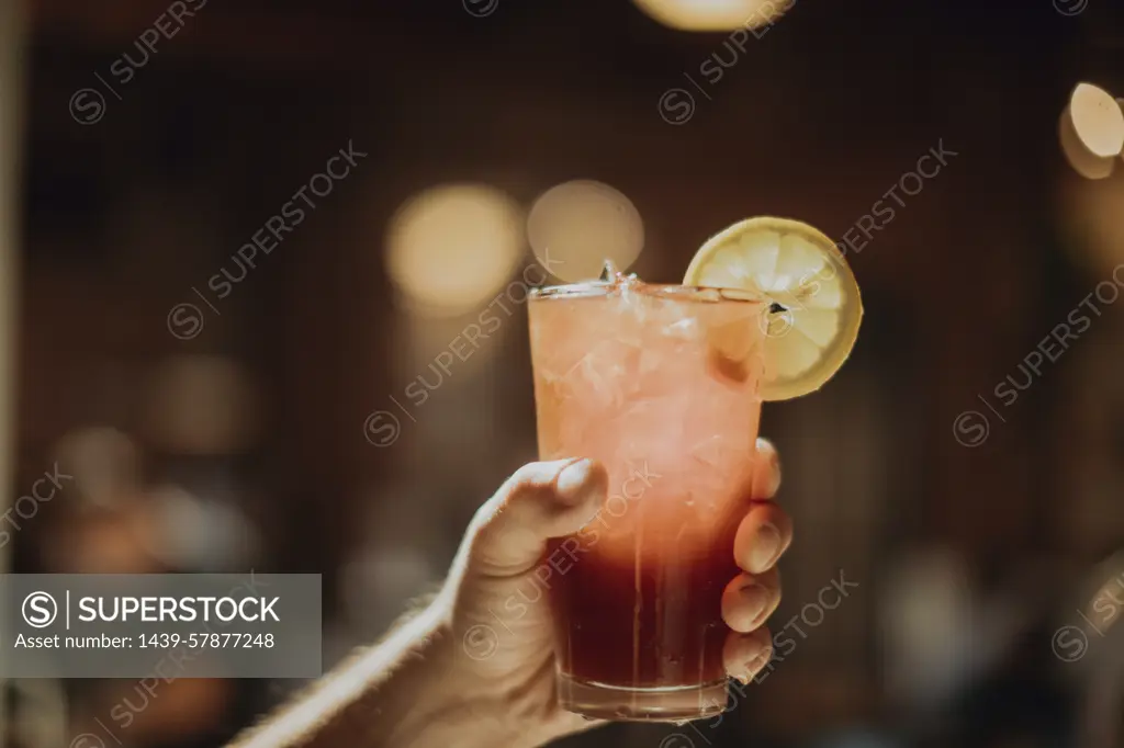 Barista holding up glass of fresh iced fruit juice in cafe, close up of hand