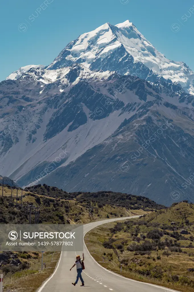 Hiker crossing road leading towards mountains, Wanaka, Taranaki, New Zealand