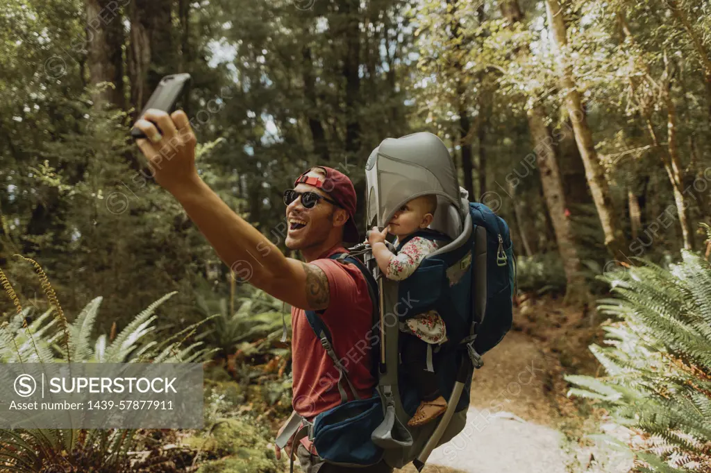 Father with baby taking selfie in forest, Queenstown, Canterbury, New Zealand