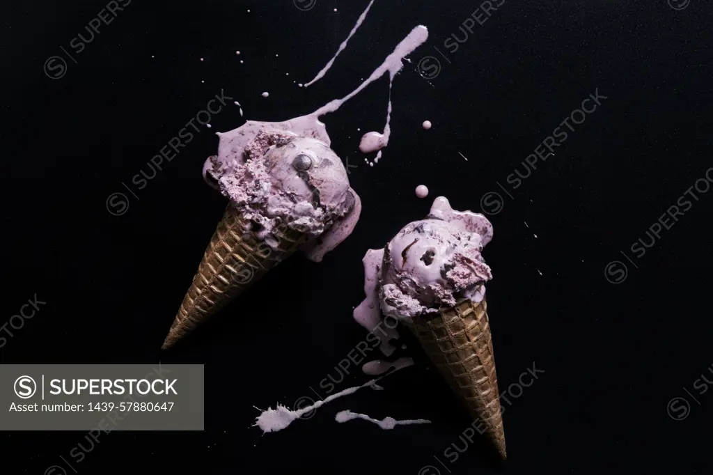 A dynamic splash with two ice cream cones mid topple against a black background