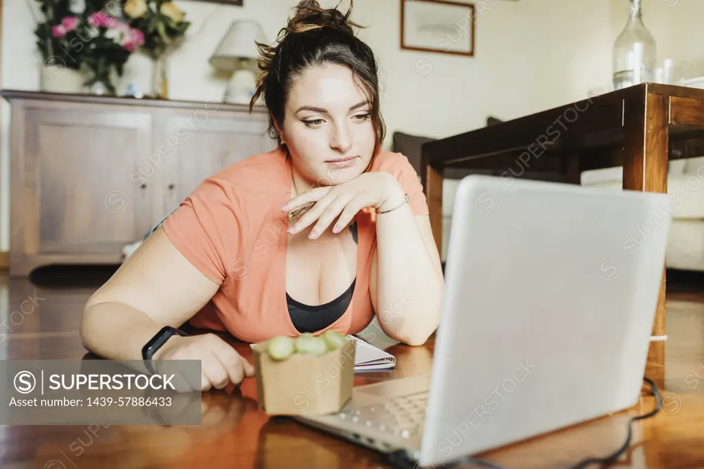 Contemplative young woman with a healthy snack taking a break from working on her laptop at home.