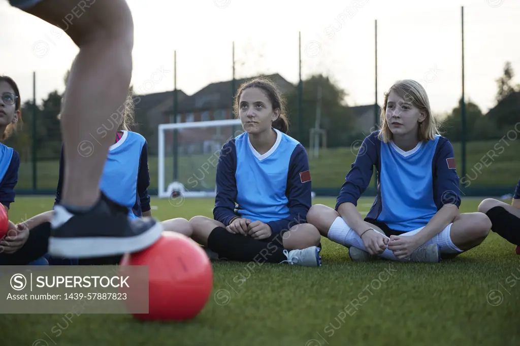 Young soccer players attentively listening to their coach at dusk