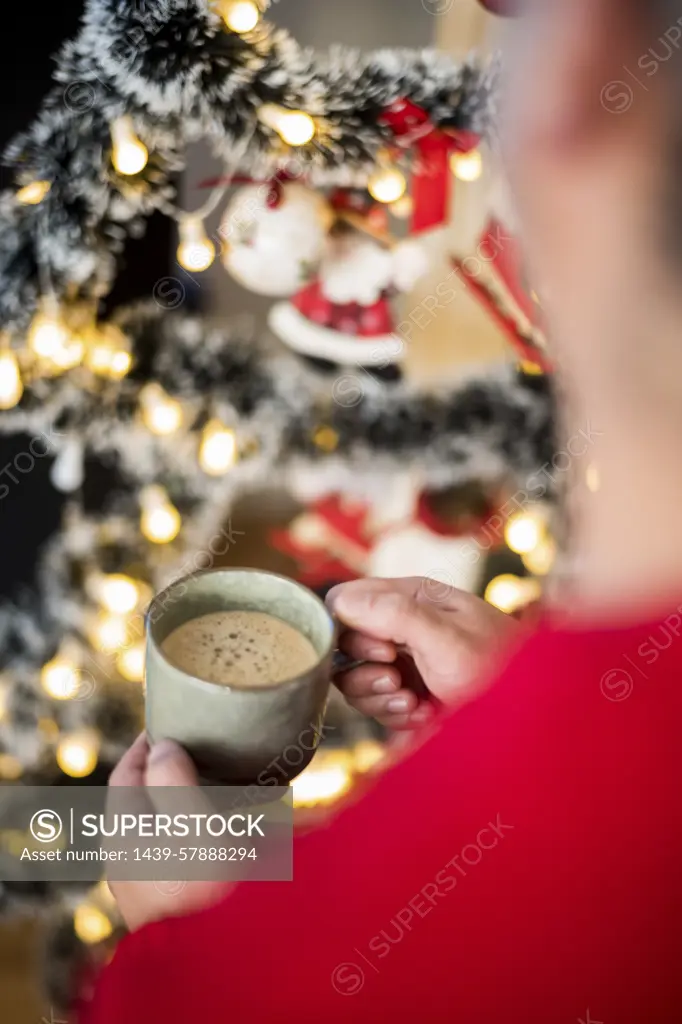 Cozy holiday moment with a warm drink in hand beside a beautifully decorated Christmas tree.