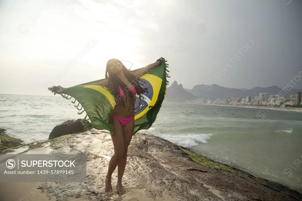 Young woman holding up Brazilian flag,  Ipanema beach, Rio De Janeiro, Brazil