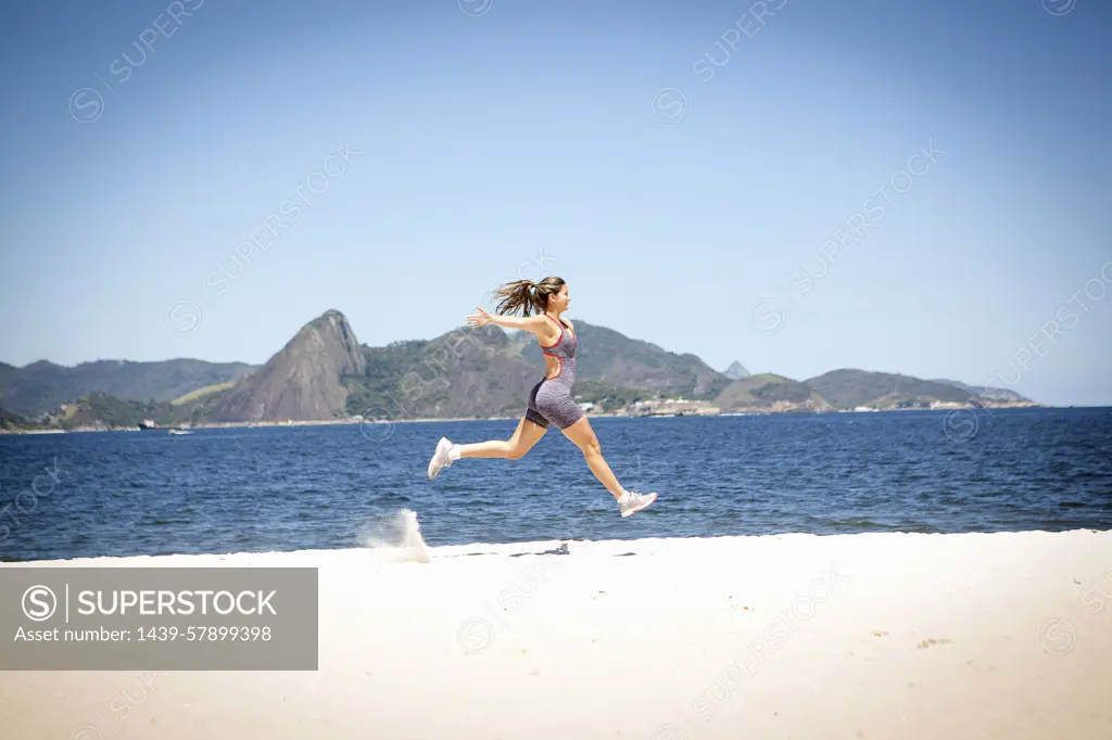 Young woman jumping on beach, Rio de Janeiro, Brazil