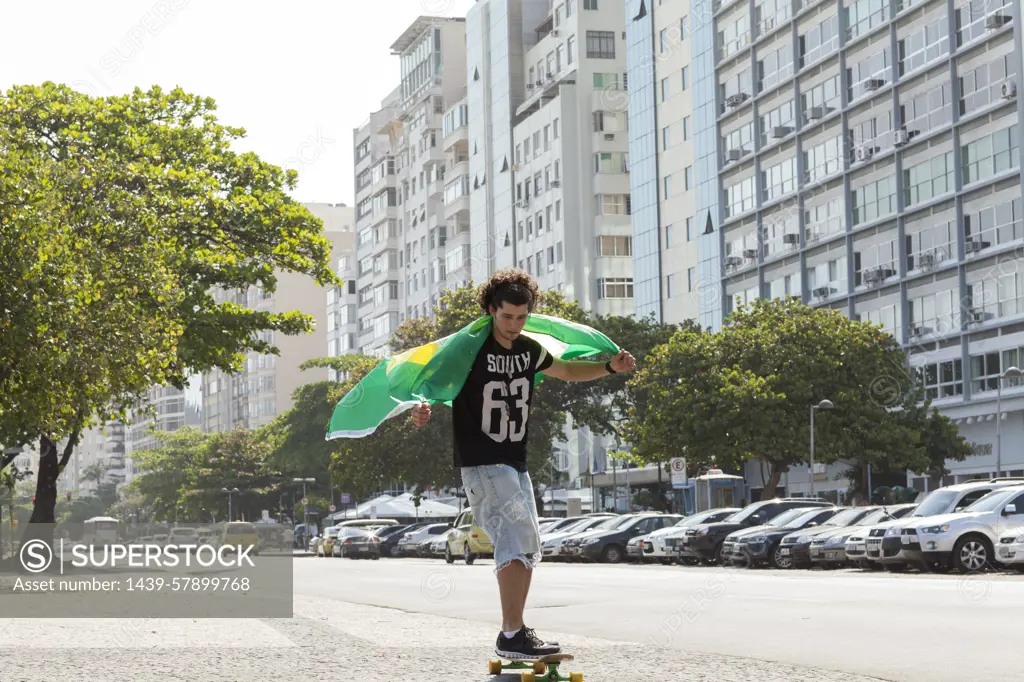 Young man skateboarding holding Brazilian flag, Copacabana, Rio De Janeiro, Brazil