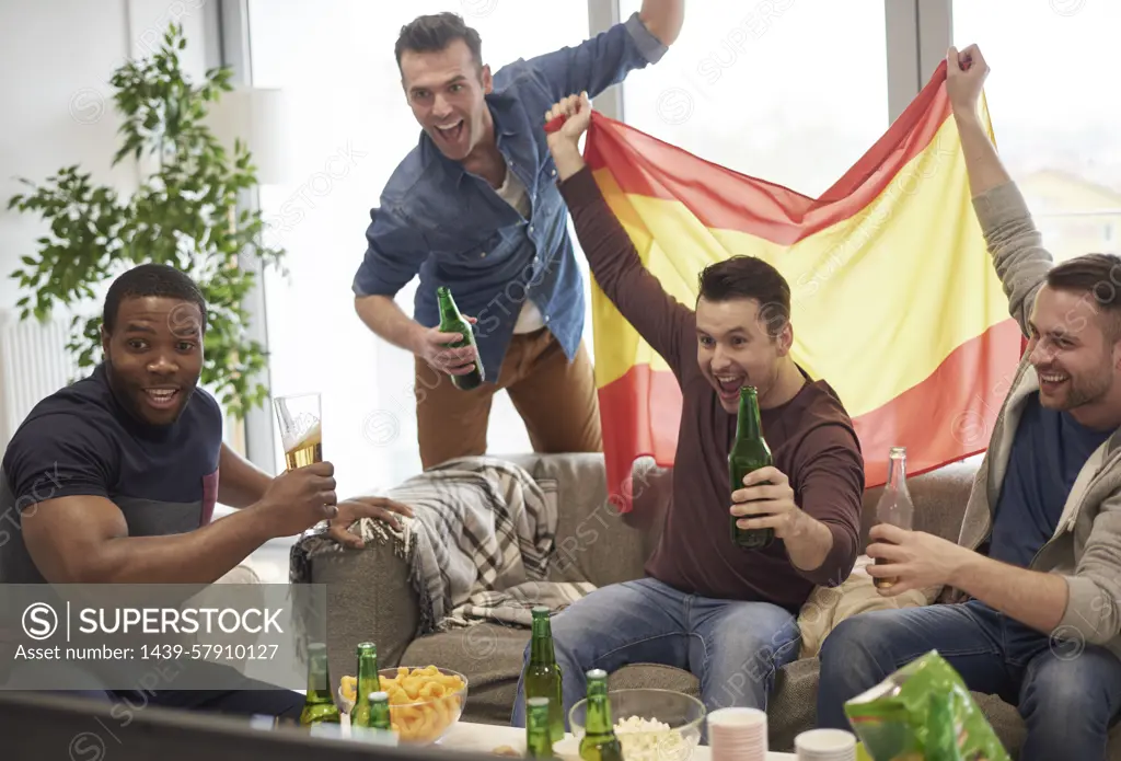 Group of men watching sporting event on television holding Spanish flag celebrating