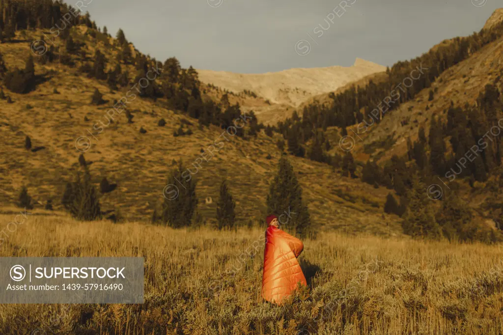 Woman standing in field, wrapped in sleeping bag, Mineral King, Sequoia National Park, California, USA