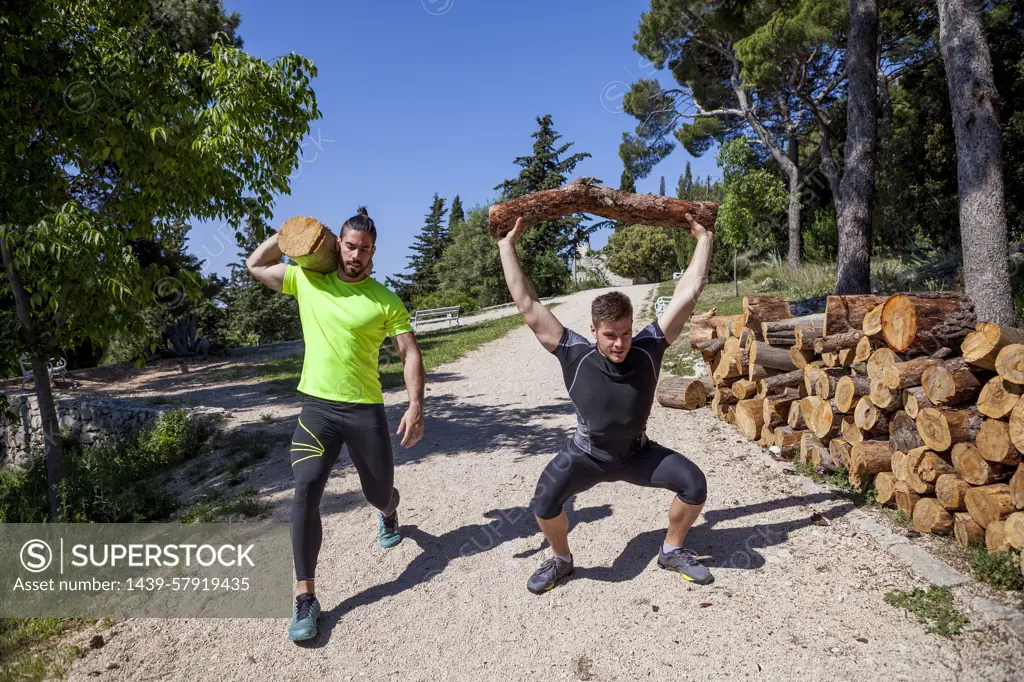 Two young men doing weightlifting training with logs in forest, Split, Dalmatia, Croatia