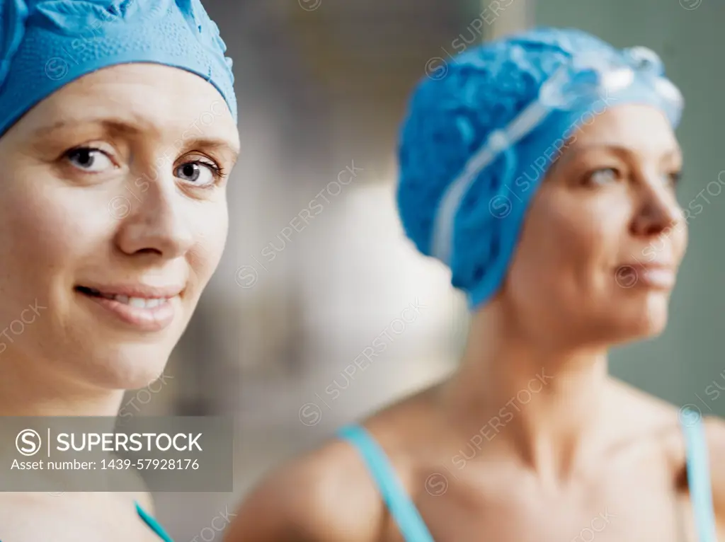 Two women wearing swimming caps and goggles smiling at the poolside