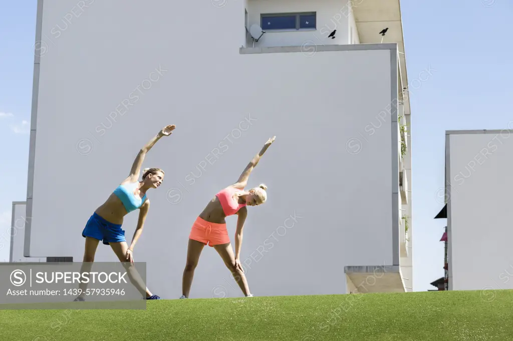 Two young female athletes stretching in park