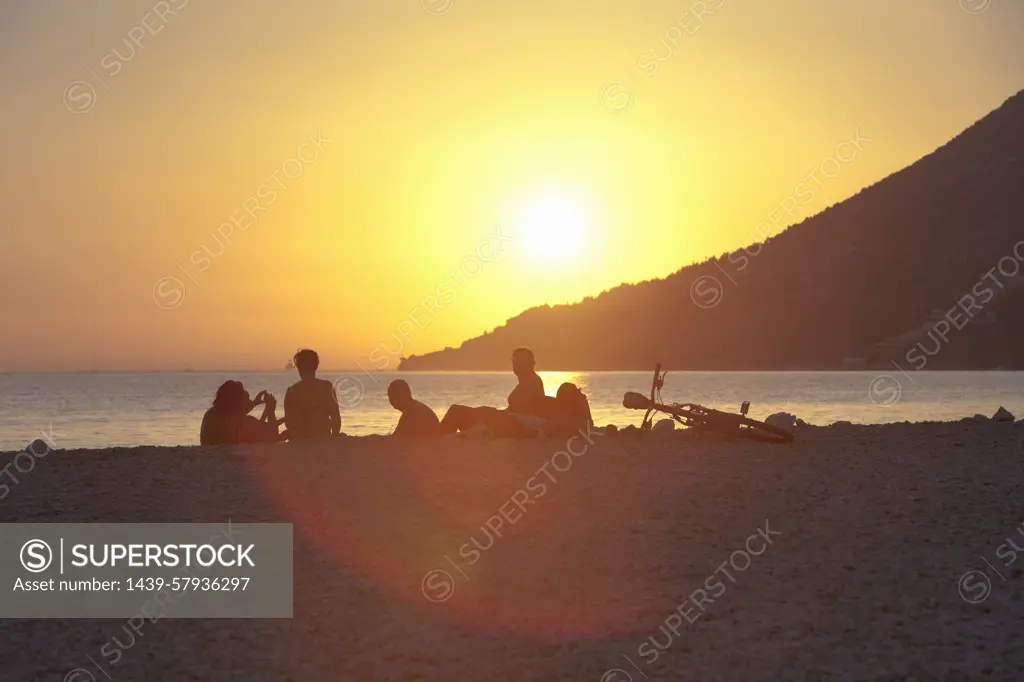 Small group of people watching sunset on beach, Vigan, Croatia