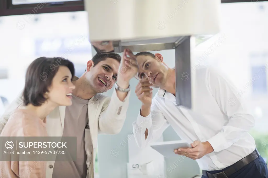 Mid adult couple and salesman looking at extractor hood in kitchen showroom