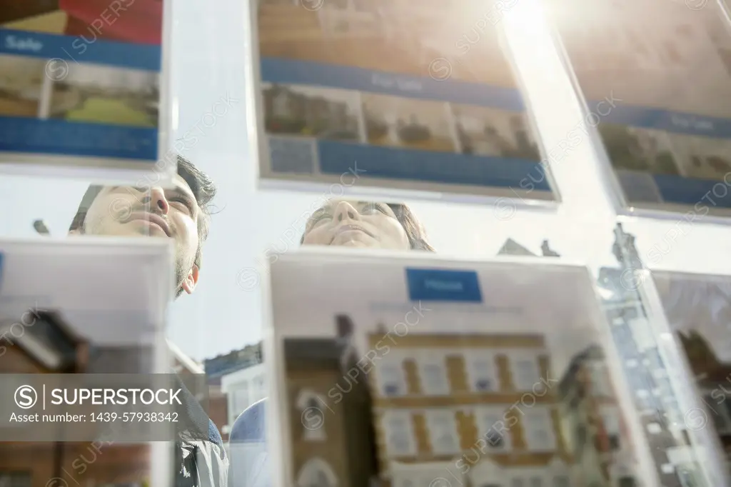 Couple contemplatively browsing real estate listings in a shop window.