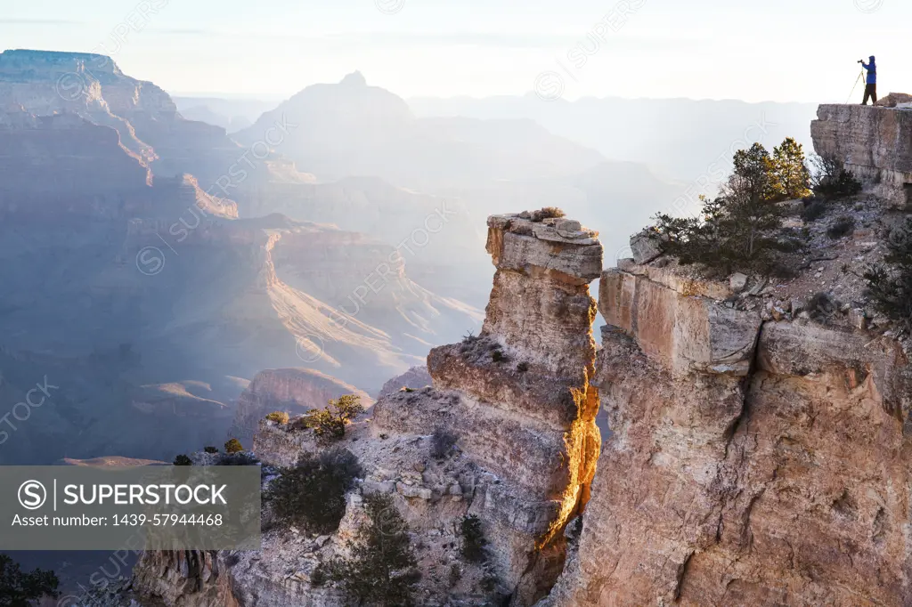 An adventurer stands atop a cliff enjoying the vast beauty of the Grand Canyon at sunrise.